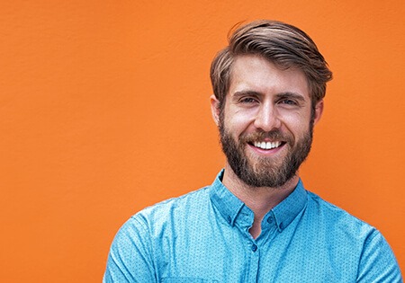 A man with a beard is smiling in front of an orange wall.